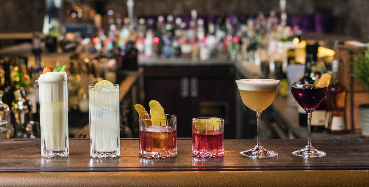 Six cocktails servis dans des verres différents sur un comptoir de bar